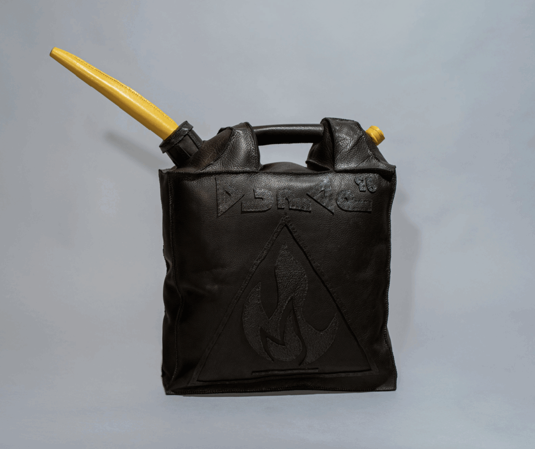 A black leather bag shaped like a fuel canister, with a yellow nozzle attached to a black cap. Embossed symbols and a flame warning sign are visible on the front.